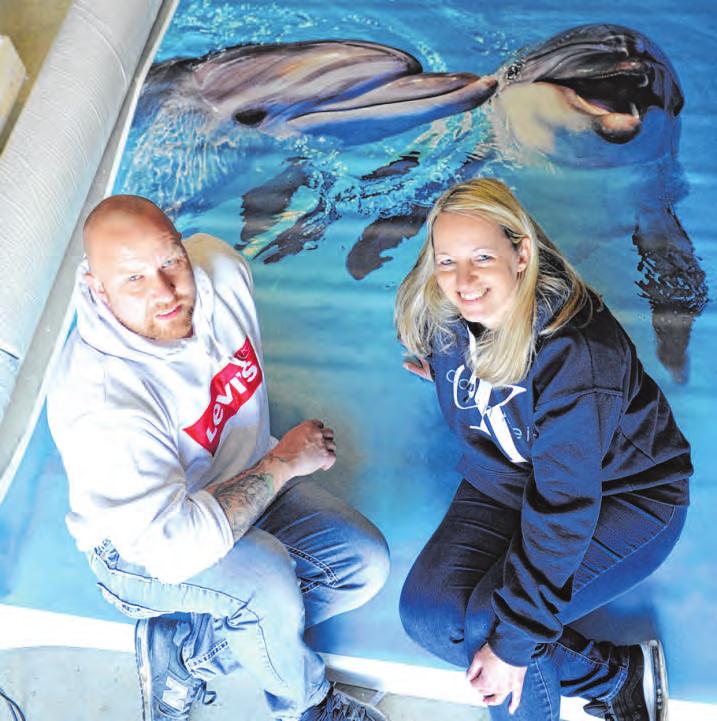 Christian Richter und Lebensgefährtin Bettina Irmler sitzen in der Werkstatt vor einem Bild mit Delfinen. Es ist eines der Motive, die sich mit einem enorm realistischen 3D-Effekt verlegen lassen. Wenn die letzte Schicht aufgetragen ist, wird es so aussehen, als ob die Flipper dem Betrachter ihre Nasen zum Streicheln entgegenstrecken. Foto: Palapies Christian Richter und Lebensgefährtin Bettina Irmler sitzen in der Werkstatt vor einem Bild mit Delfinen. Es ist eines der Motive, die sich mit einem enorm realistischen 3D-Effekt verlegen lassen. Wenn die letzte Schicht aufgetragen ist, wird es so aussehen, als ob die Flipper dem Betrachter ihre Nasen zum Streicheln entgegenstrecken. Foto: Palapies